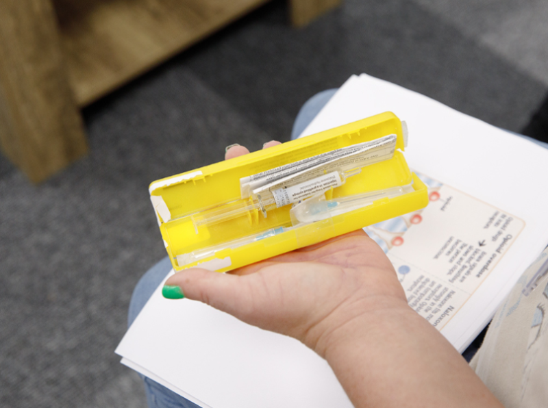 Close of a hand holding a yellow naloxone injection kit